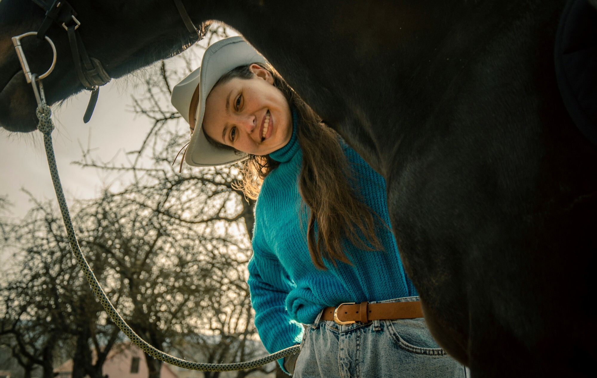 A woman smiling standing with her hand resting on a horse